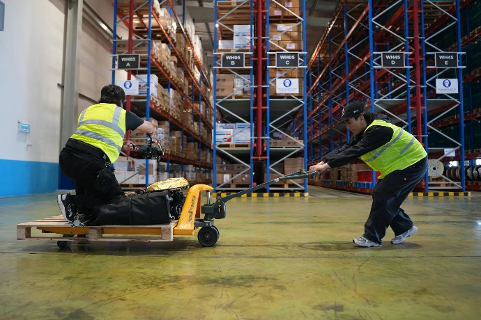 Two workers moving pallet with hand truck in warehouse